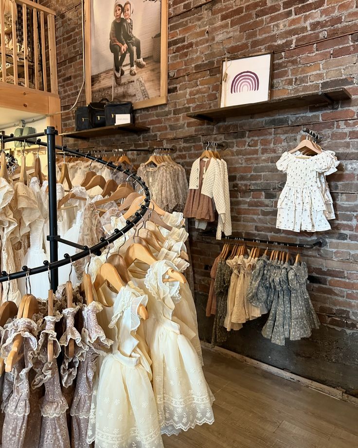 there are many dresses and shoes on display in the store with brick wall behind them