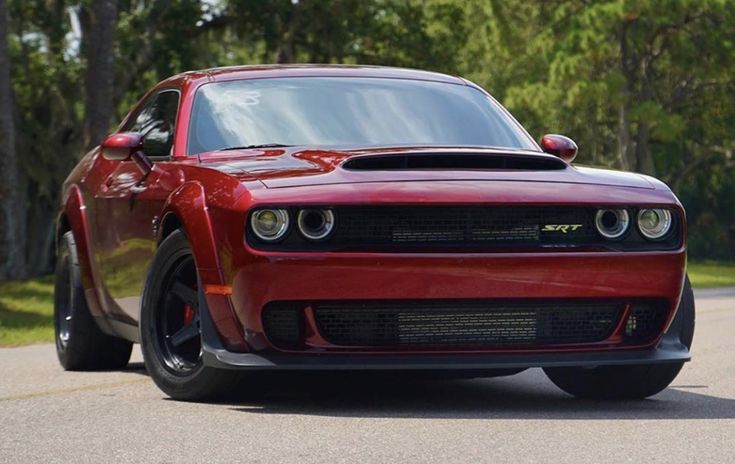 the front end of a red sports car driving on a road near trees and grass