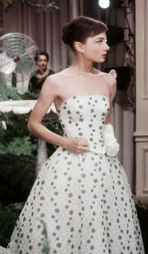 a woman in a white and black dress standing next to a christmas tree with people behind her