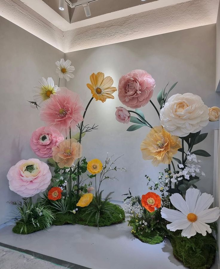 an arrangement of flowers on display in a room with white walls and green mossy flooring