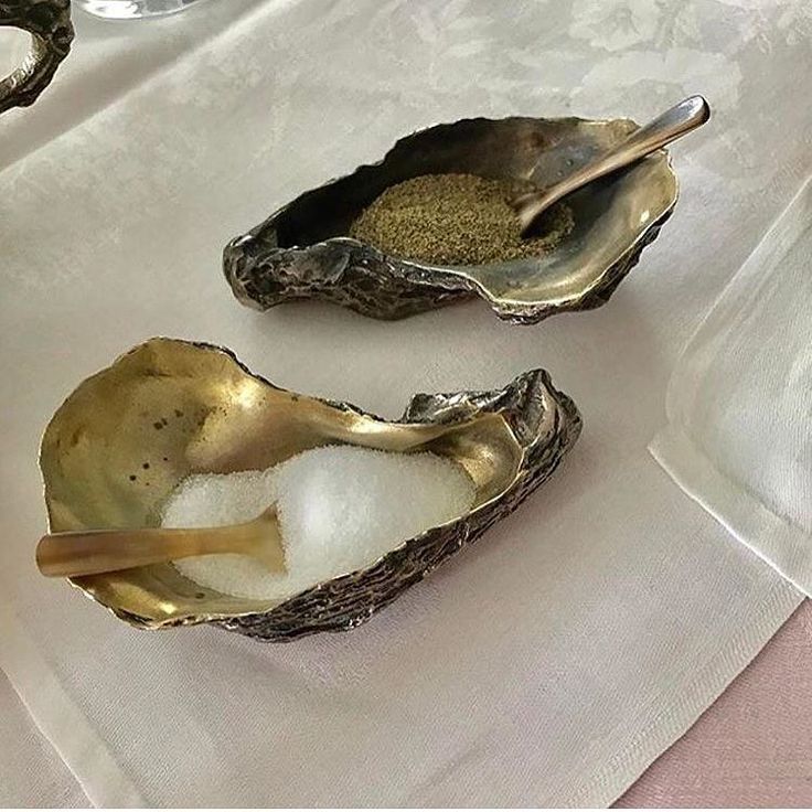 three oysters with salt and pepper in them on a white table cloth next to silverware