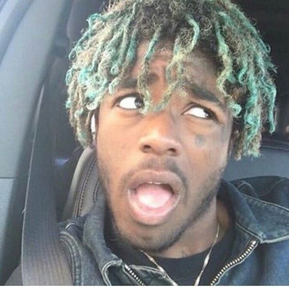 a young man with dreadlocks sticking his tongue out in the back seat of a car