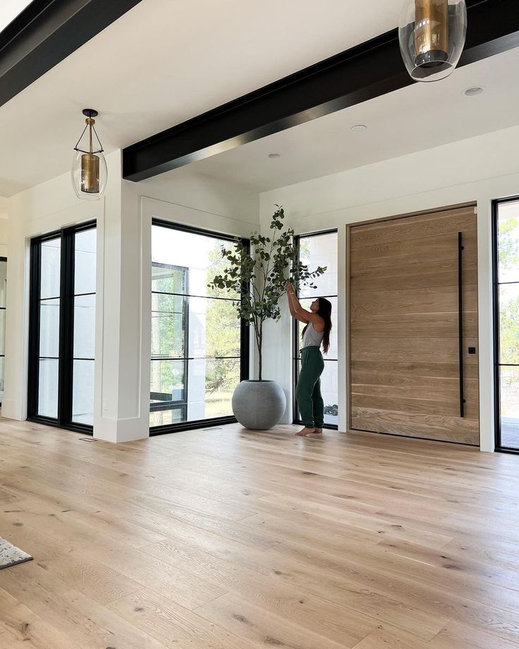 a woman is standing in the middle of a room with wood floors and large windows