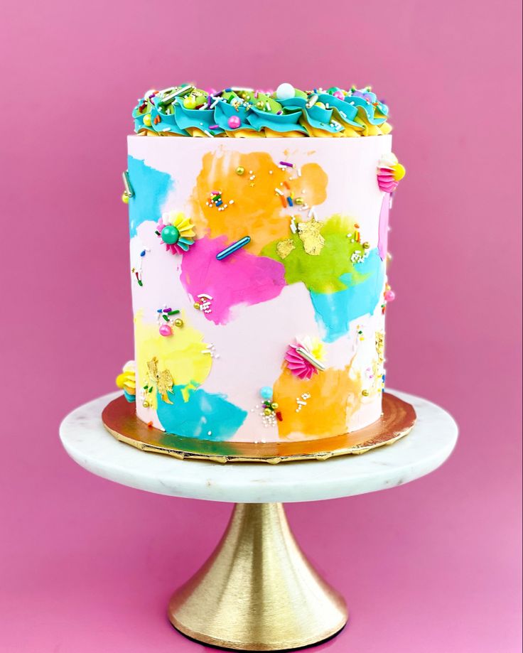 a multicolored cake with sprinkles on top sits on a gold pedestal