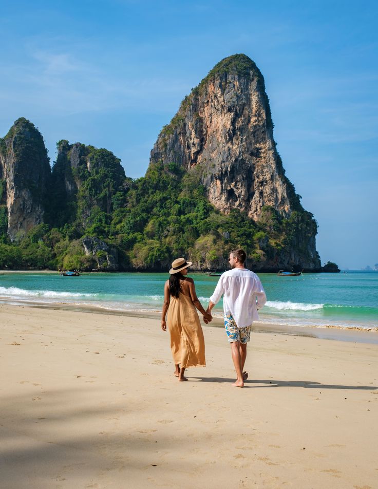 a man and woman walking on the beach holding hands