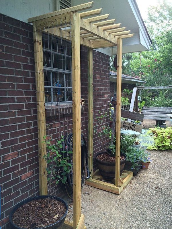 a wooden trellis next to a brick building with potted plants on the porch