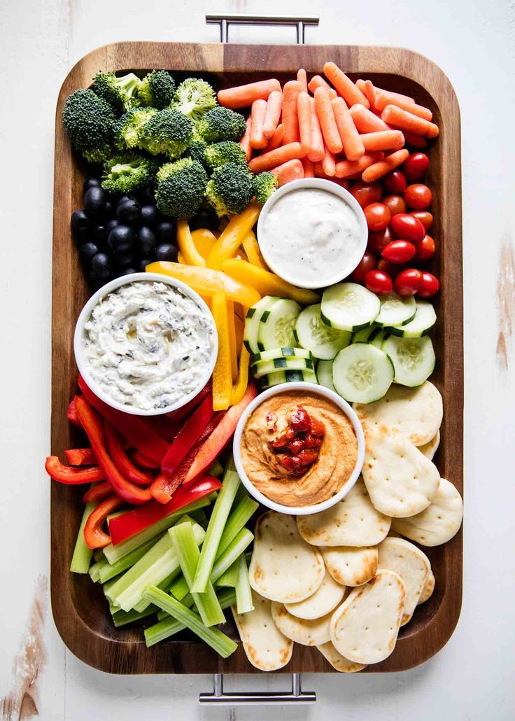 a platter filled with veggies, crackers, dips and vegetables