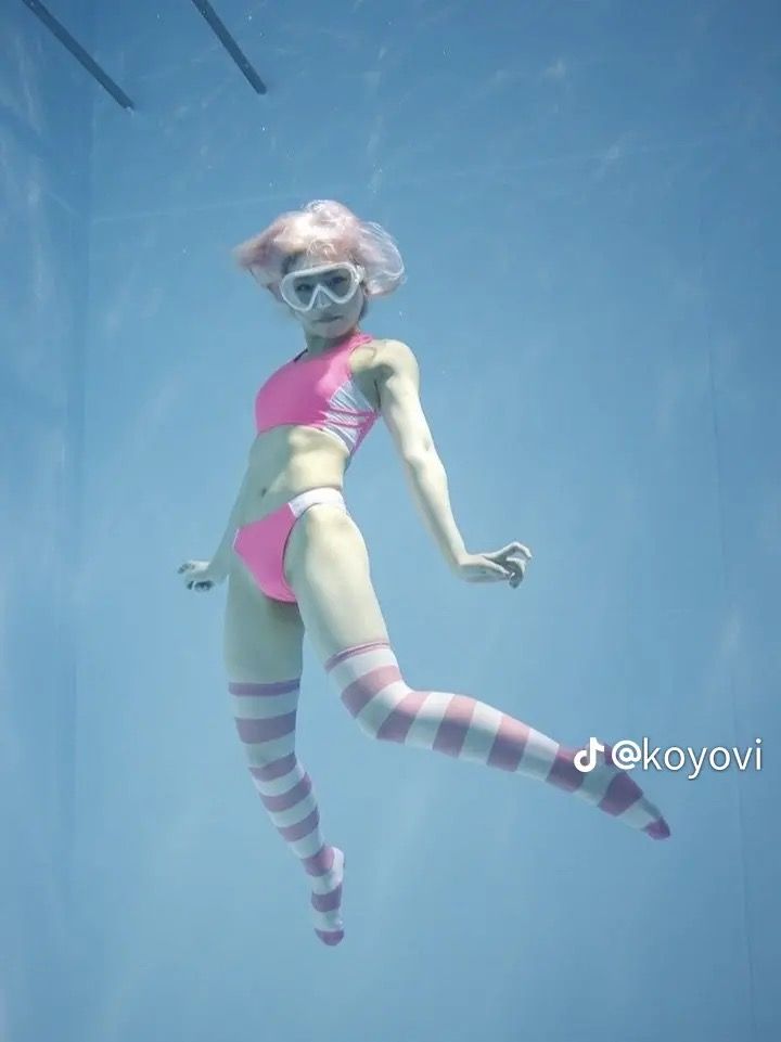 a woman in pink swimsuit and striped stockings diving under water