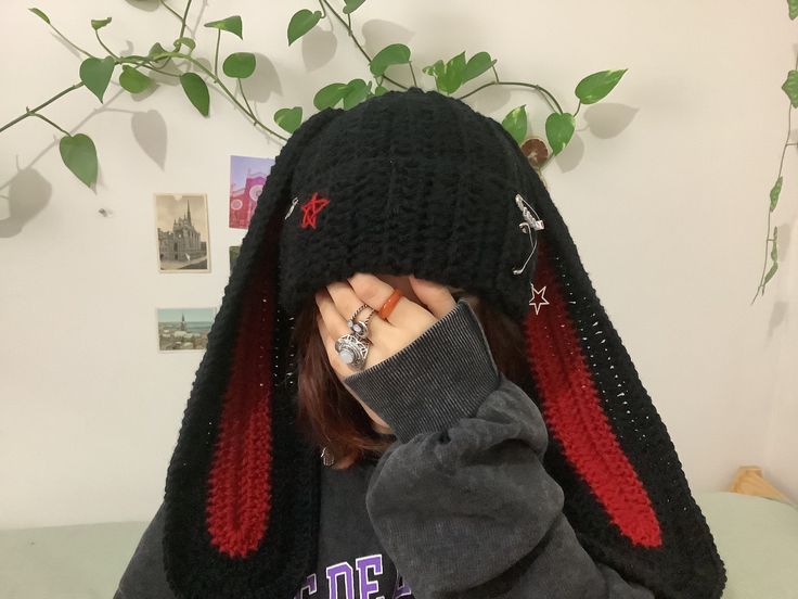 a woman covering her face with a black and red knitted rabbit hat on top of her head