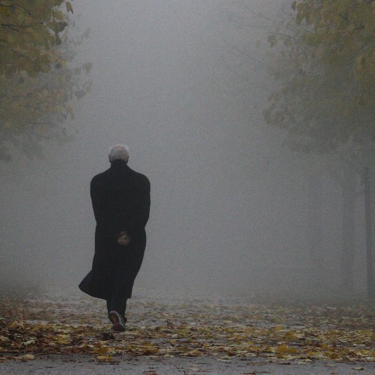 a man walking down a street in the fog with an umbrella over his head and coat on