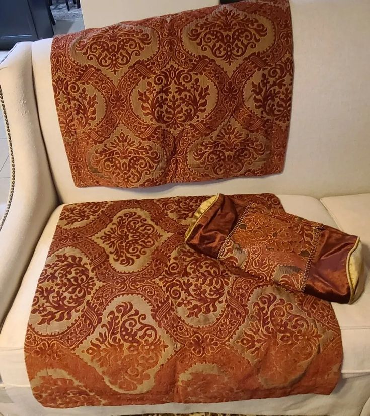 an orange and gold blanket sitting on top of a white couch next to a pillow