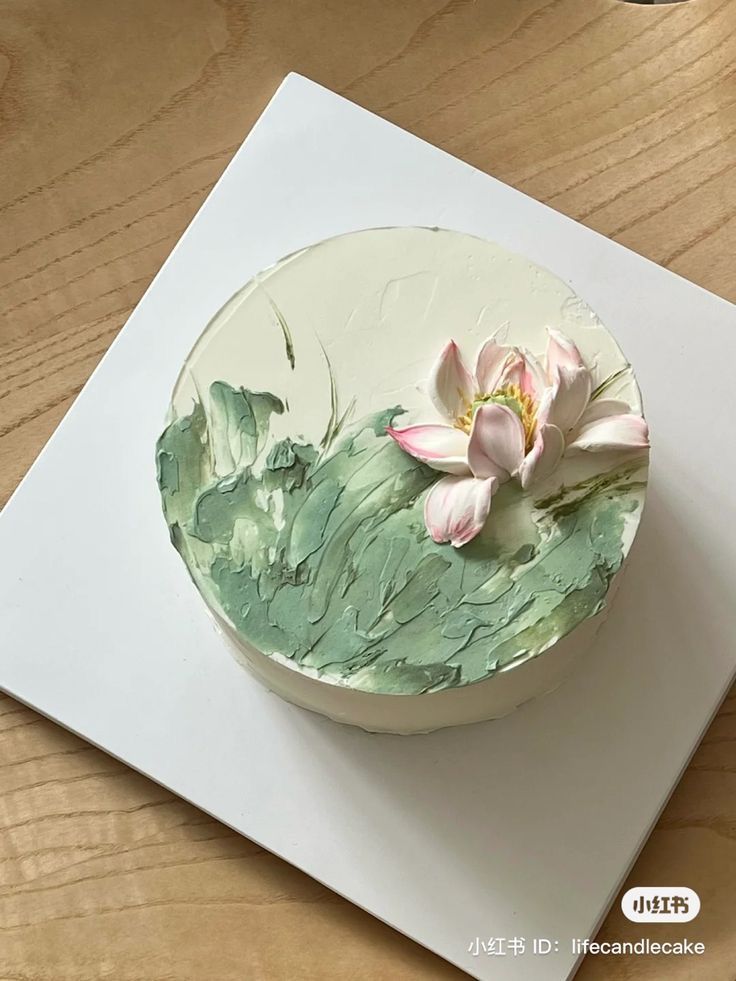 a white cake with green icing and pink flowers on the top is sitting on a wooden table