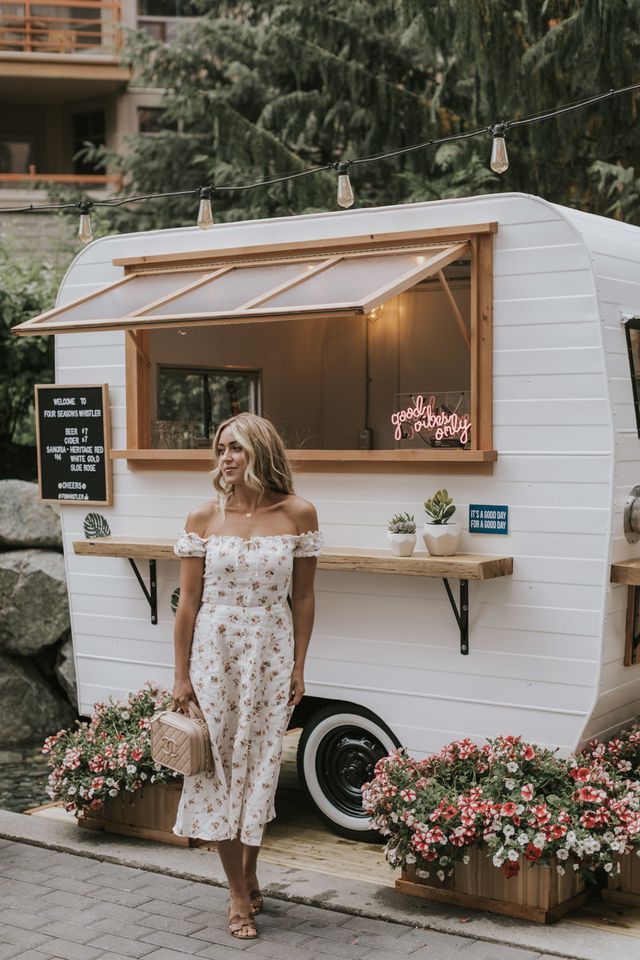 a woman standing in front of a food truck with potted plants on the side