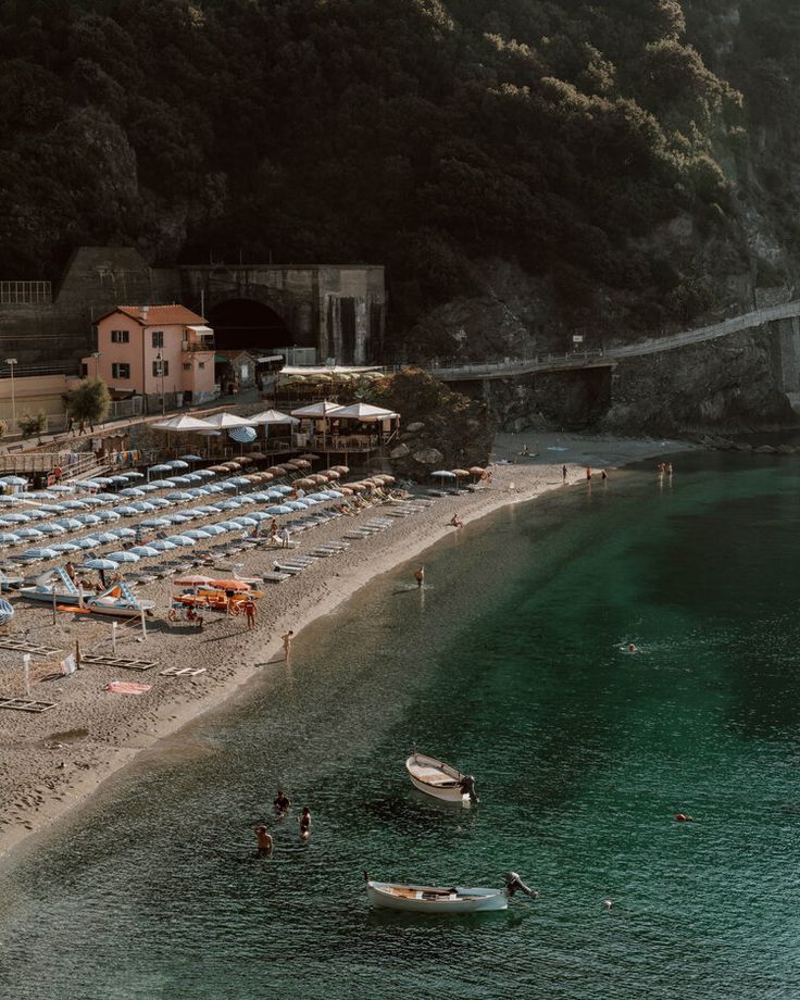 the beach is lined with umbrellas and chairs next to an old stone bridge over water