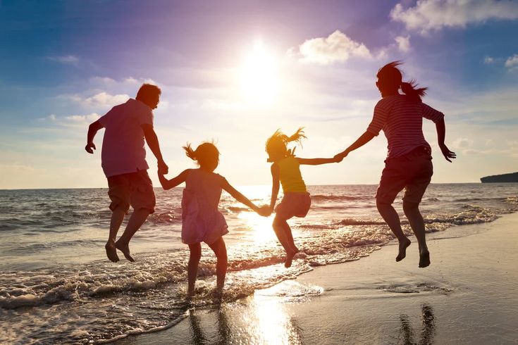 four people jumping in the air at the beach with their arms around each other as they run into the water