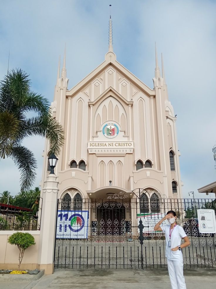 a woman standing in front of a church with palm trees around her and a fence surrounding it