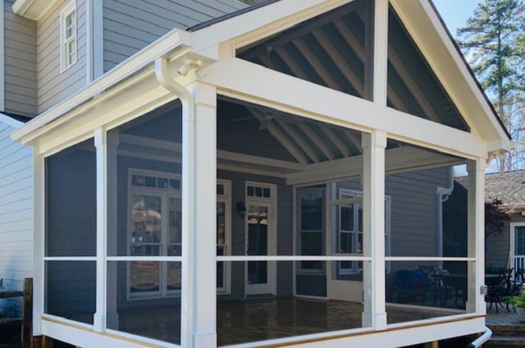 a screened porch in front of a house with gray siding and white trim on it