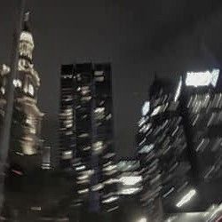 blurry photograph of city skyline at night with skyscrapers in the foreground and cars driving by