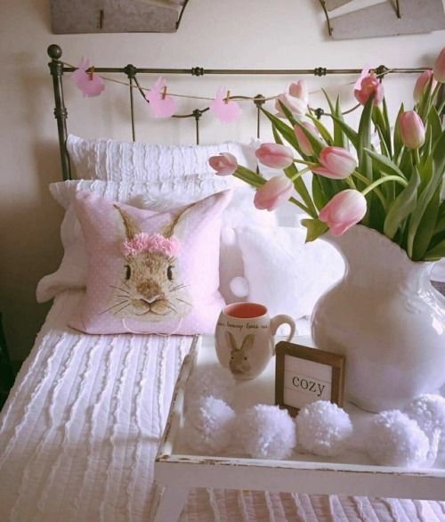 a white bed topped with pink flowers next to a vase filled with tulips