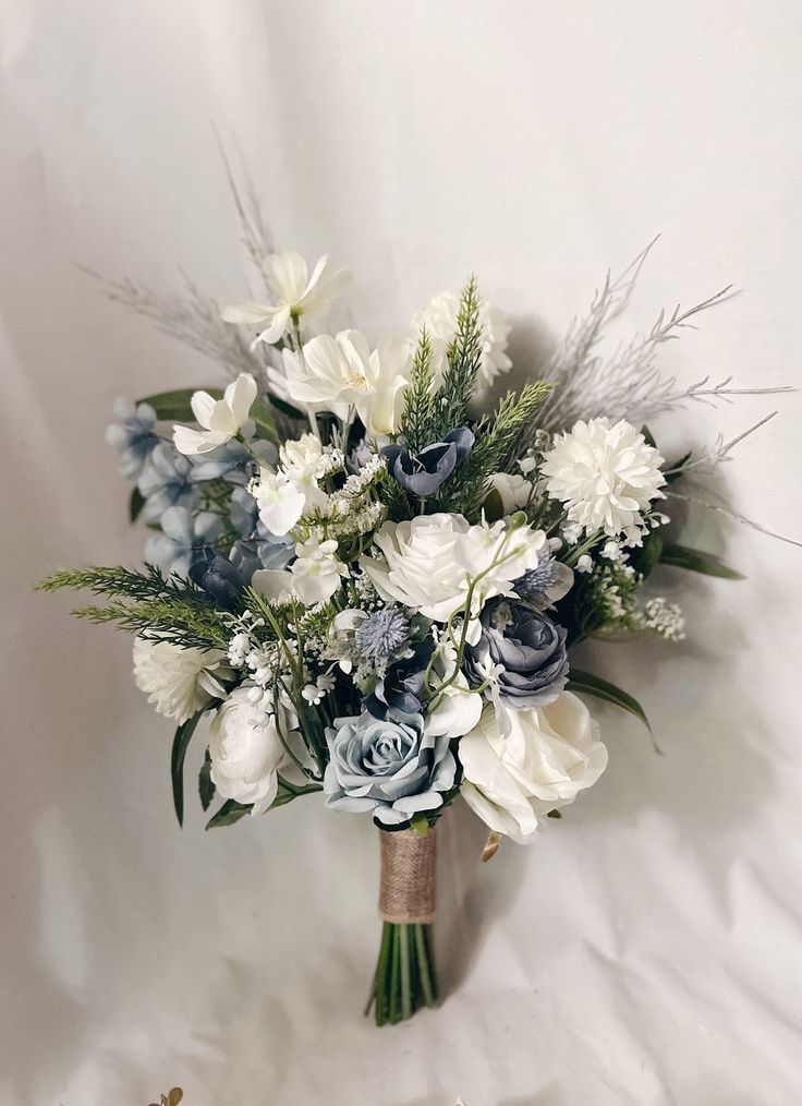 a bridal bouquet with blue and white flowers on a white cloth background for a wedding or special occasion