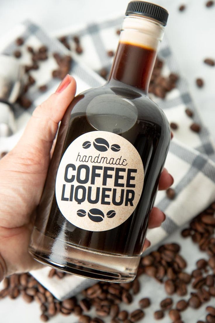 a hand holding a bottle of coffee liqueur surrounded by coffee beans on a checkered cloth