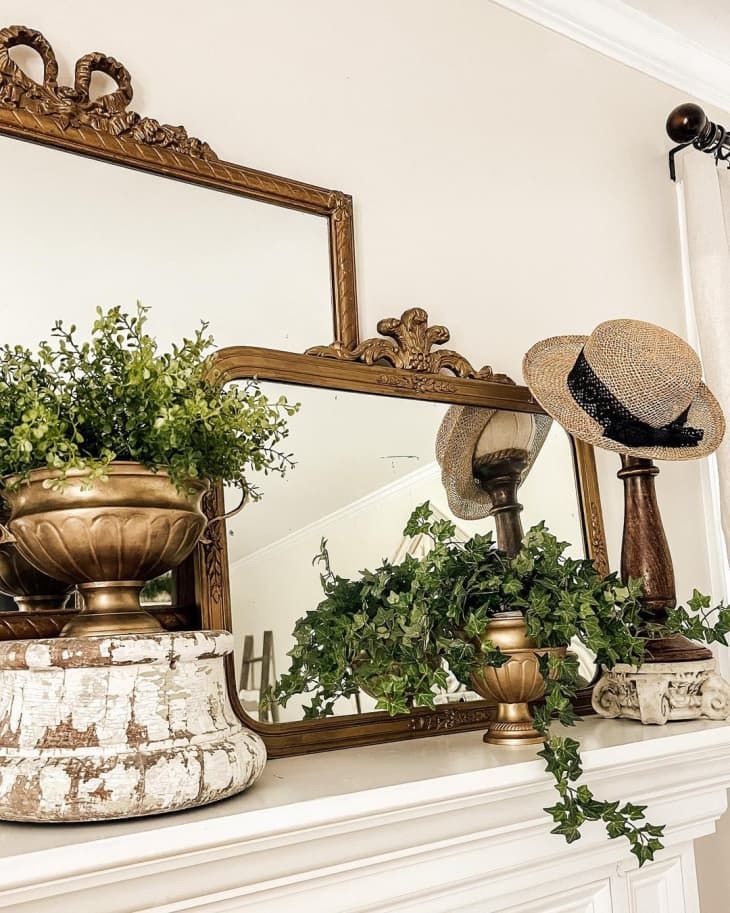 there is a mirror, potted plants and a hat on top of the mantle