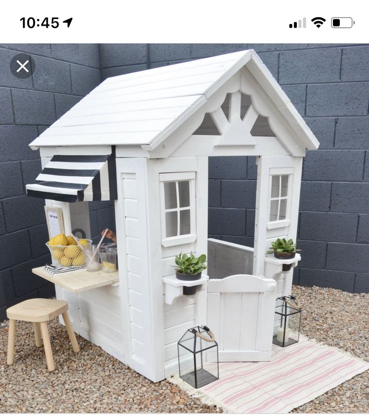 a small white house sitting on top of a gravel ground next to a wooden table