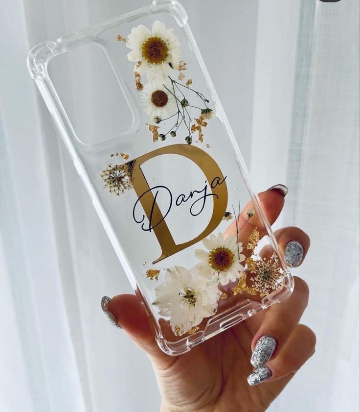 a person holding up a clear phone case with flowers on it and the letter d