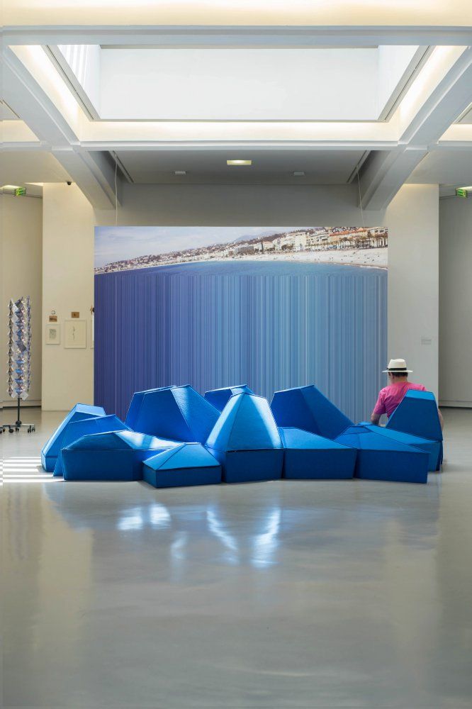 a blue couch sitting on top of a white floor next to a tall building with a skylight