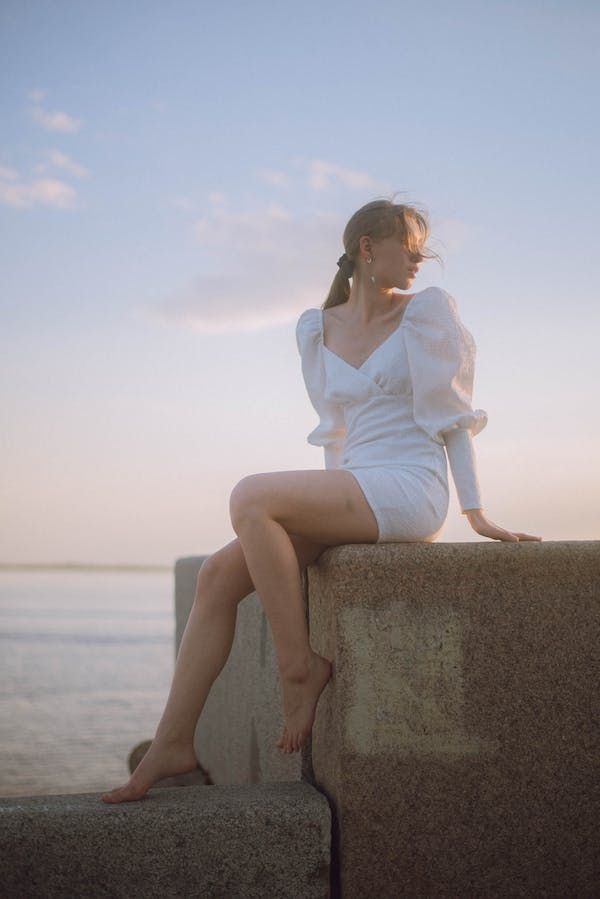 a woman sitting on top of a stone wall next to the ocean with her legs crossed