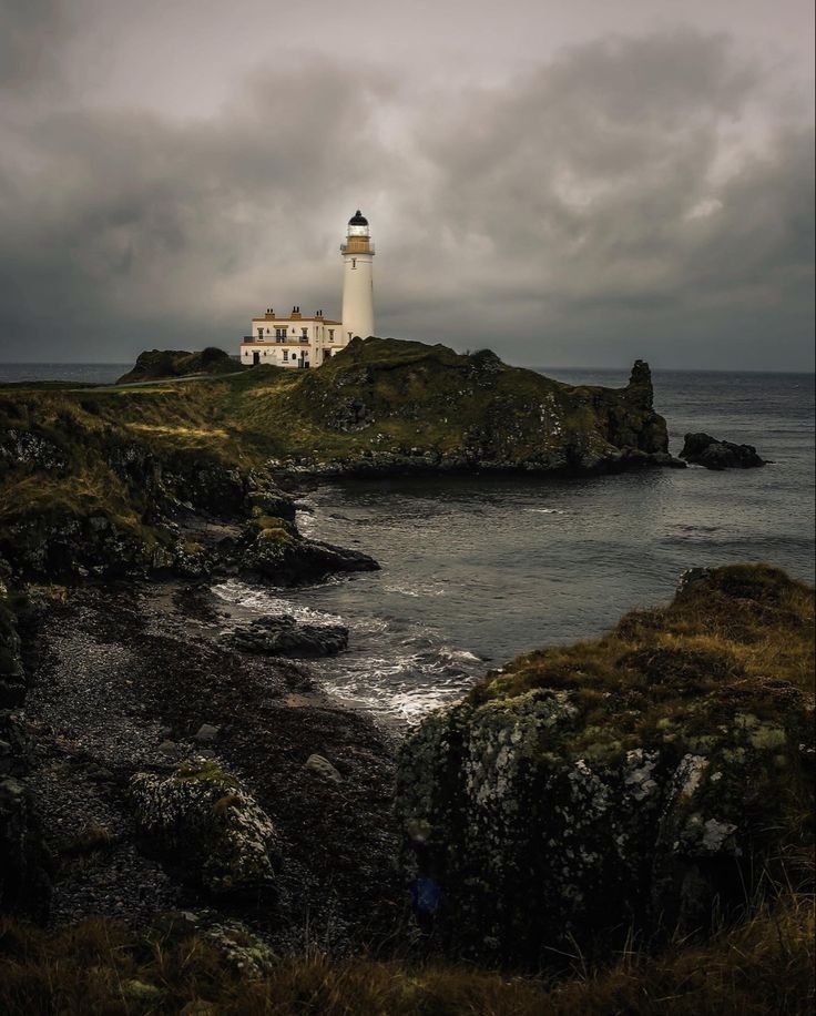 a lighthouse on an island in the middle of the ocean with dark clouds above it