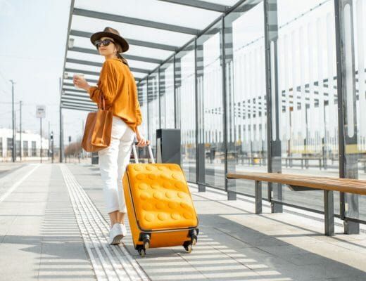 a woman in an orange top pulling a yellow suitcase