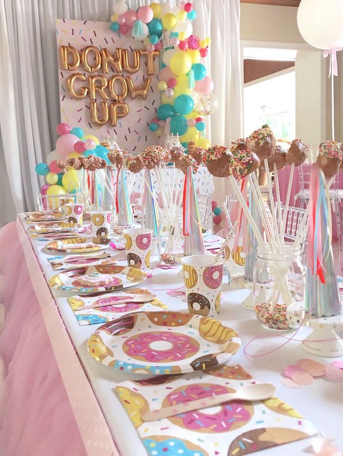 a table is set up for a donut party with balloons and confetti