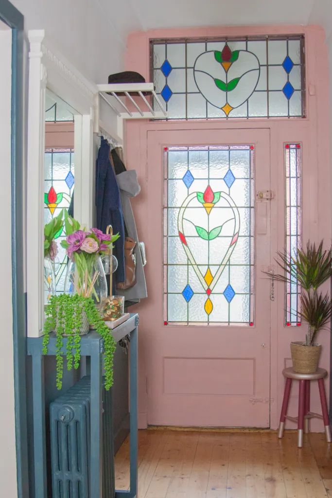 a pink front door with stained glass and potted plants next to it on a wooden floor