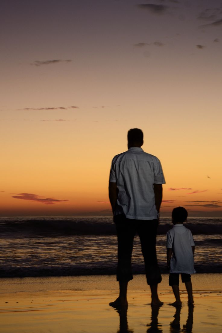 a man and child standing on the beach at sunset