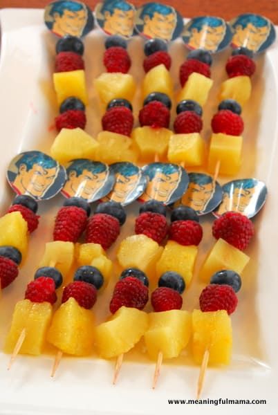 fruit skewers are arranged on a plate with silver spoons and blueberries