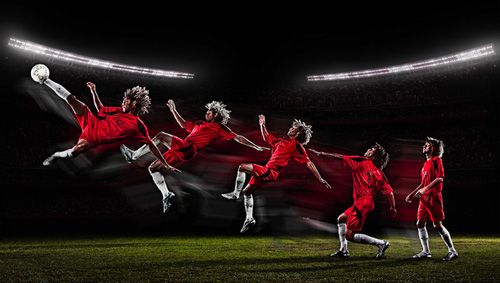 a group of soccer players in action on the field at night with bright lights behind them