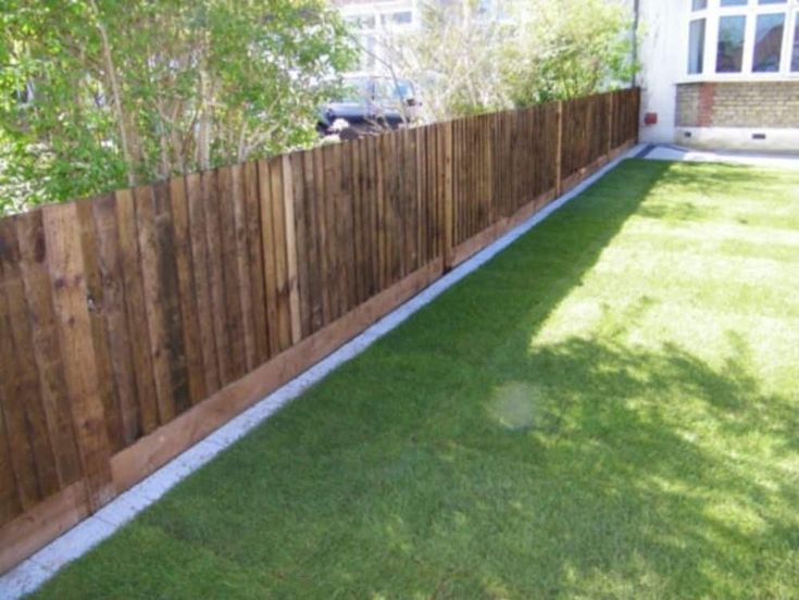 a wooden fence in front of a house with grass on the ground and a car parked behind it