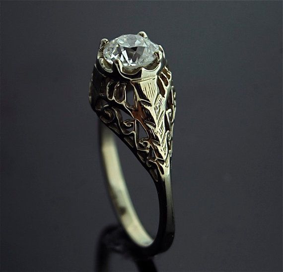 a ring with a diamond in the center on a black surface and an intricate design around it