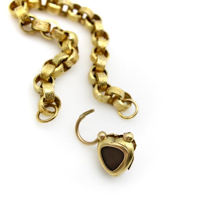 This is part of Chairish’s Fine Jewelry assortment.  Circa the 1840’s, the centerpiece of this 14k gold bracelet is a heart shape padlock clasp with a garnet carbuncle. The oval cabochon has a high profile and blood red glow—the gold backing behind the stone gives it a warm luminescence that shines through as the stone moves in the light. The garnet is prong set and surrounded by a viney leaf motif that intertwines with the prongs and is reminiscent of Sleeping Beauty’s rose garden labyrinth. Th 14k Gold Oval Link Jewelry With Box Clasp, Luxury Oval Link Jewelry With Gold Clasp, Timeless Yellow Gold Jewelry With Box Clasp, Heirloom Gold Jewelry With Box Clasp, Elegant Bronze Heart-shaped Jewelry, Elegant Heart-shaped Bronze Jewelry, Heirloom Style Yellow Gold Jewelry With Box Clasp, 14k Yellow Gold Jewelry With Clasp, Antique Yellow Gold Jewelry With Box Clasp