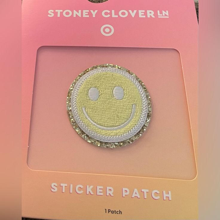 a yellow smiley face brooch sitting on top of a pink package with the words sticker patch