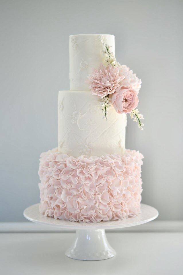 a three tiered cake with pink flowers on top and white frosting, sitting on a pedestal