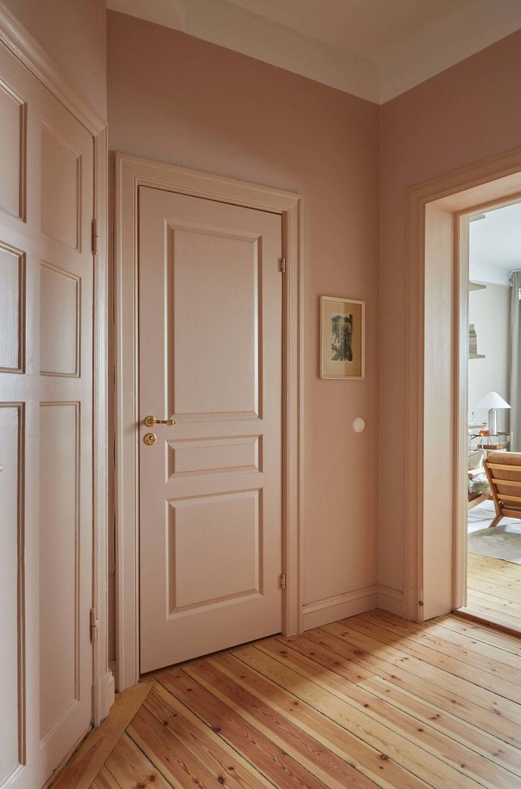 an empty room with wooden floors and two doors leading to another room that has pink walls