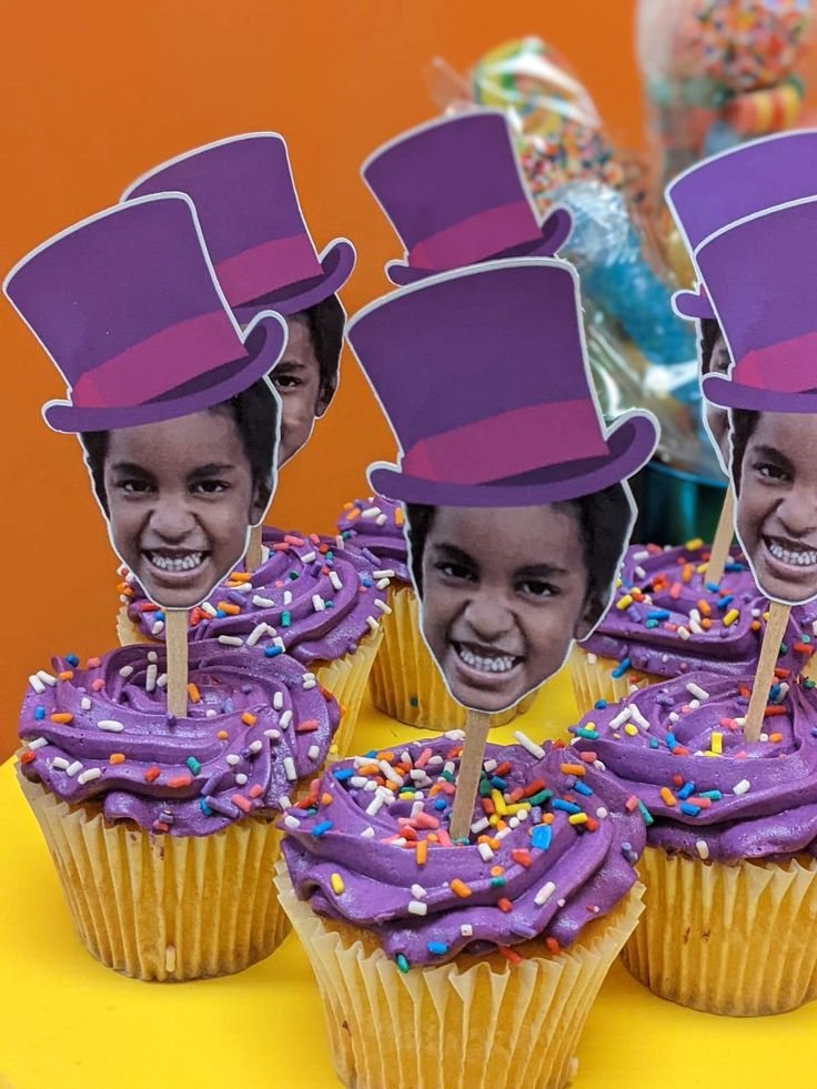 three cupcakes with purple frosting and top hats on them are sitting on a yellow table