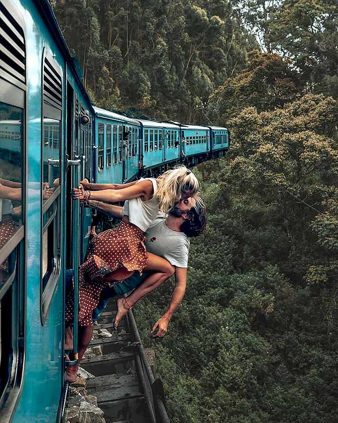 two people climbing up the side of a blue train with trees in the back ground