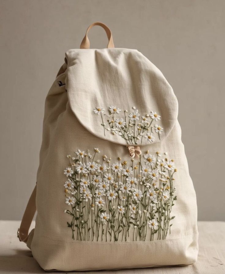 a white backpack with daisies embroidered on the front and back pocket, sitting on a table