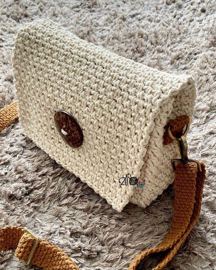 a white crocheted purse sitting on top of a gray carpet next to a brown strap