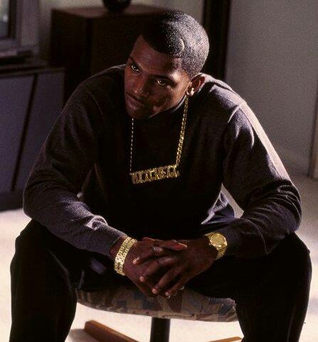 a man sitting on top of a wooden table next to a tv set and wearing a necklace