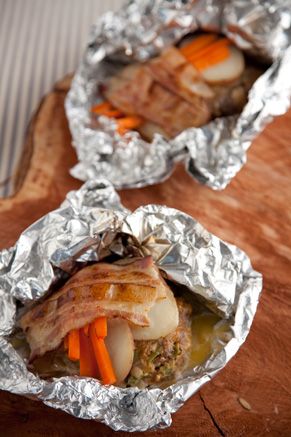 two aluminum foil wrapped sandwiches with carrots and meat in them on a wooden table