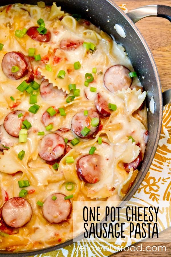 a skillet filled with pasta, sausage and cheese on top of a wooden table